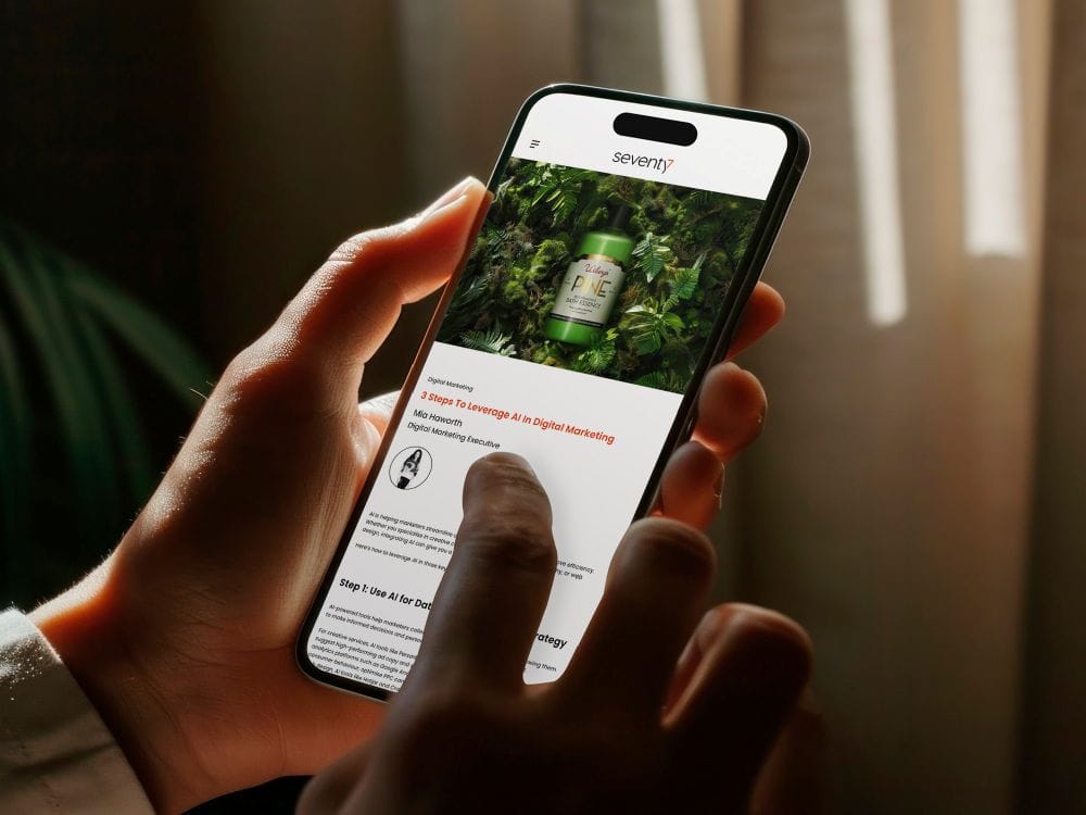 Person's hands holding a mobile phone featuring a Seventy7 blog on the screen.